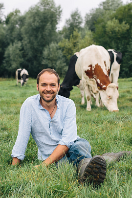 a person sitting on the grass with cows behind him